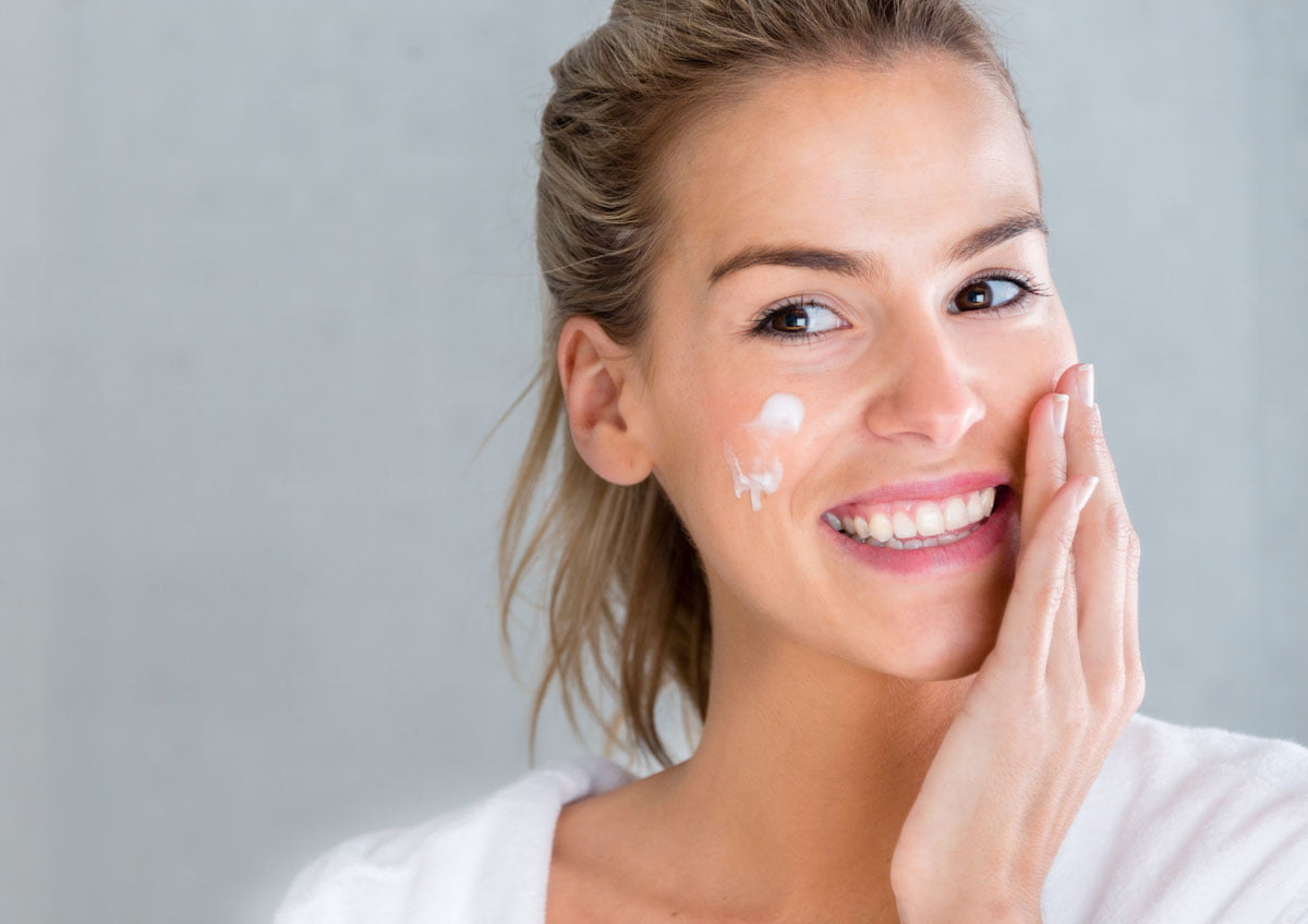 smiling woman applying cream to cheeks